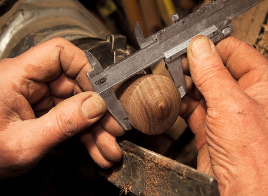 Mains d'artisan mesurant une pièce de bois au pied à coulisse